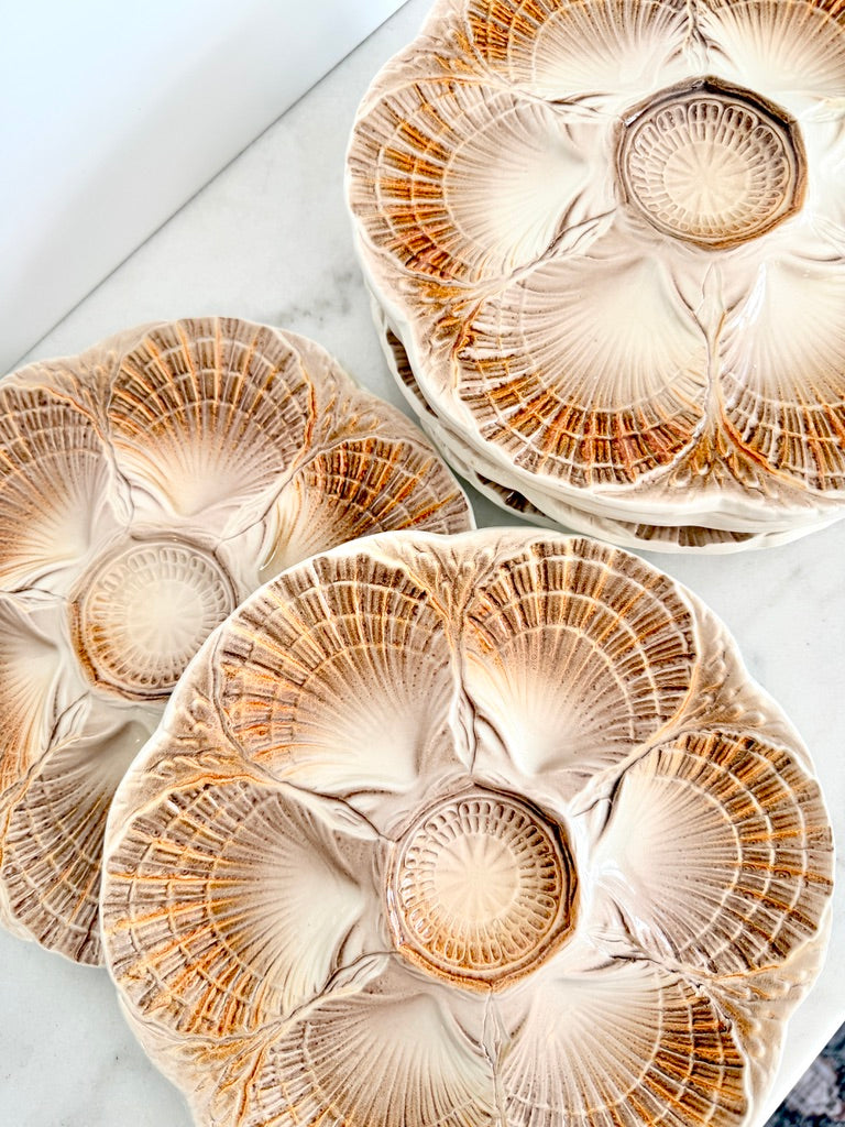 Three round ceramic plates with a textured, fan-like floral pattern in beige, cream, and brown, arranged on a light marble surface.