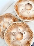 Three round ceramic plates with a textured, fan-like floral pattern in beige, cream, and brown, arranged on a light marble surface.
